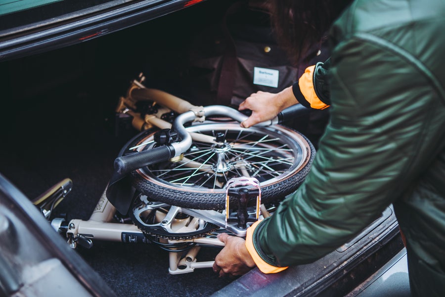 A folded Barbour x Brompton bike in the trunk of a car