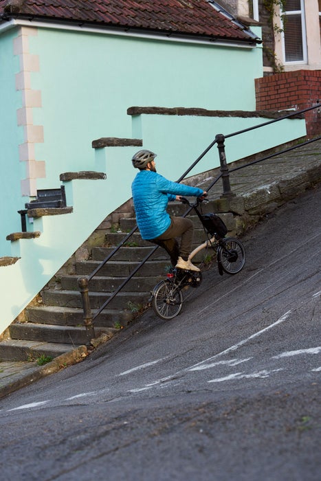 person wheeling a brompton electric folding p line bike in front of sky scraper buildings