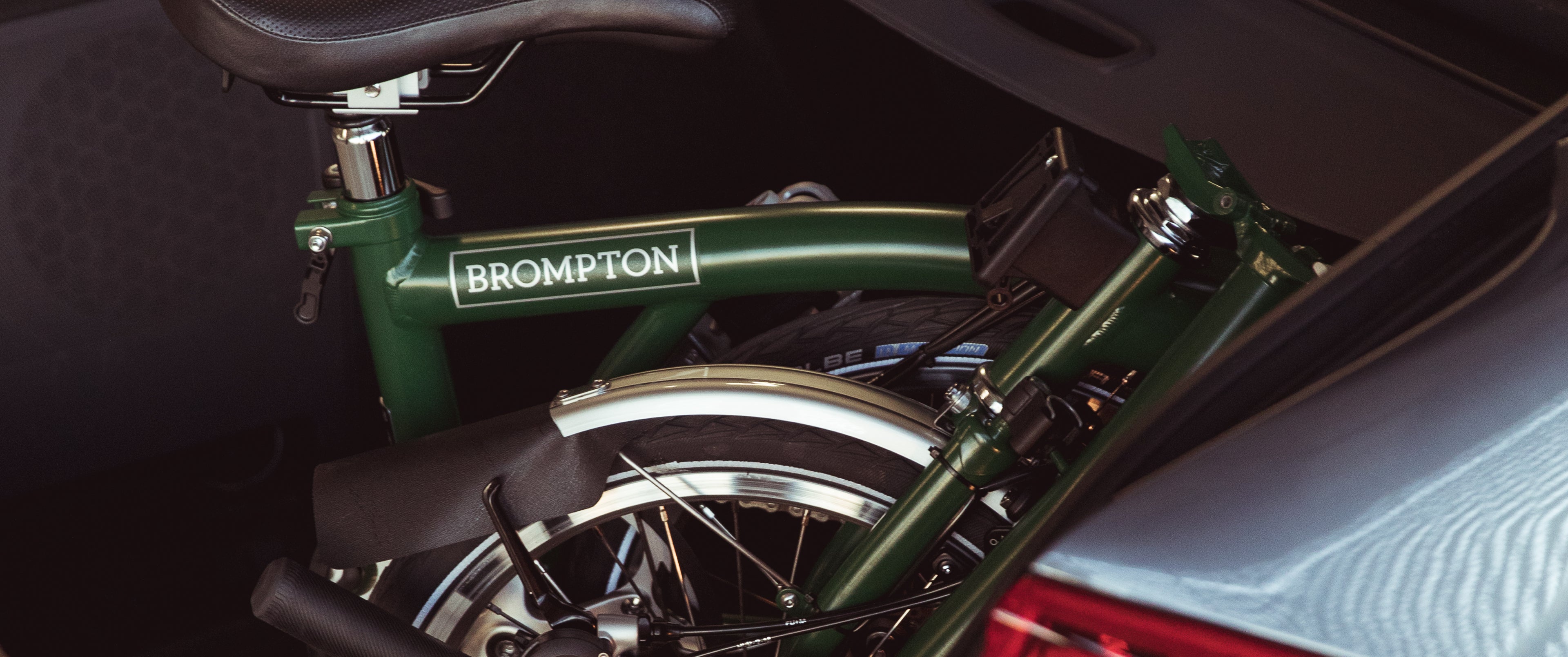 A close-up image of a forest green Brompton C Line folded in the trunk of a car