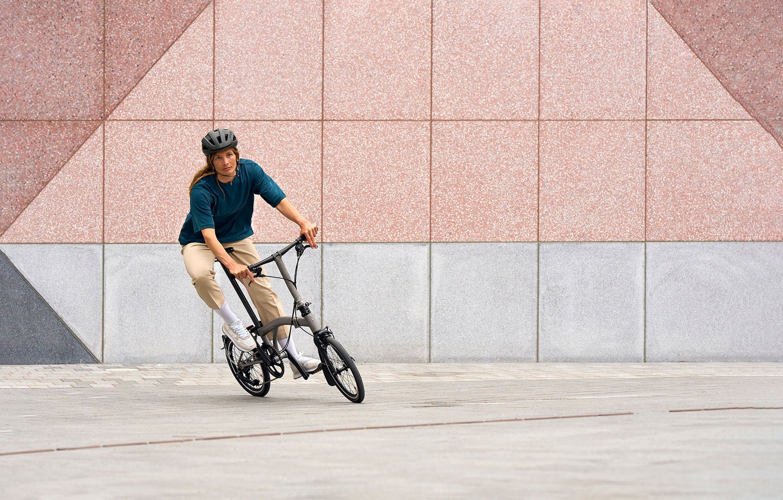 person riding a brompton t line bike in front of pink wall