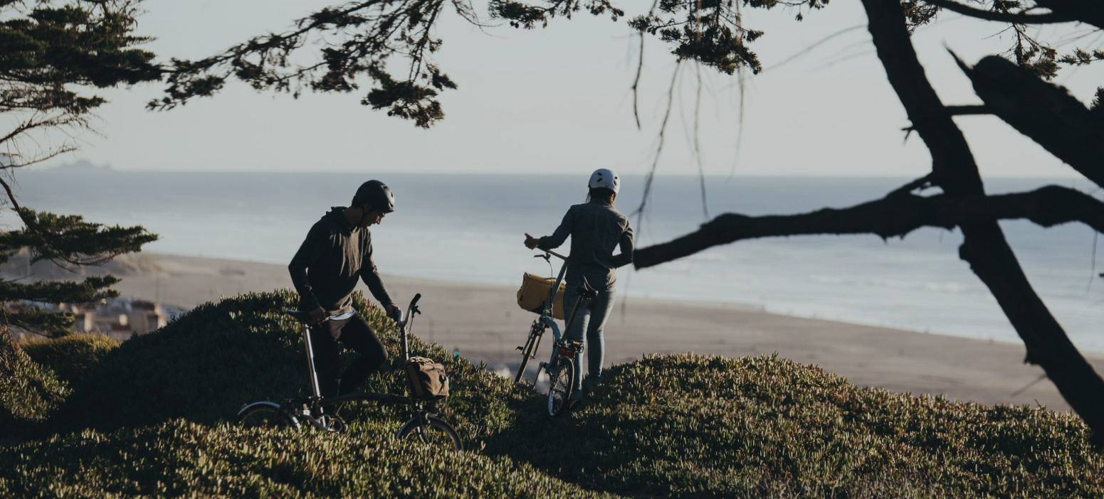 Ein Bild von zwei Radfahrern mit ihren Bromptons entlang des Strandes