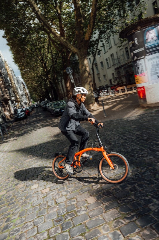 Person riding a Brompton on a cobbled street