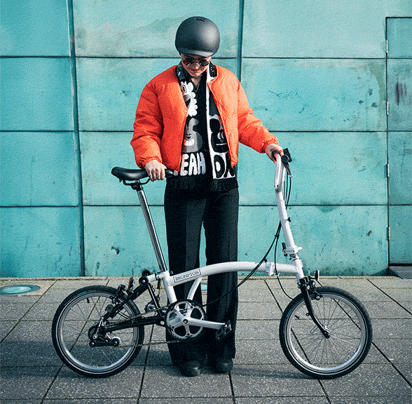 A gif of a person in an orange jacket folding down a Brompton A Line