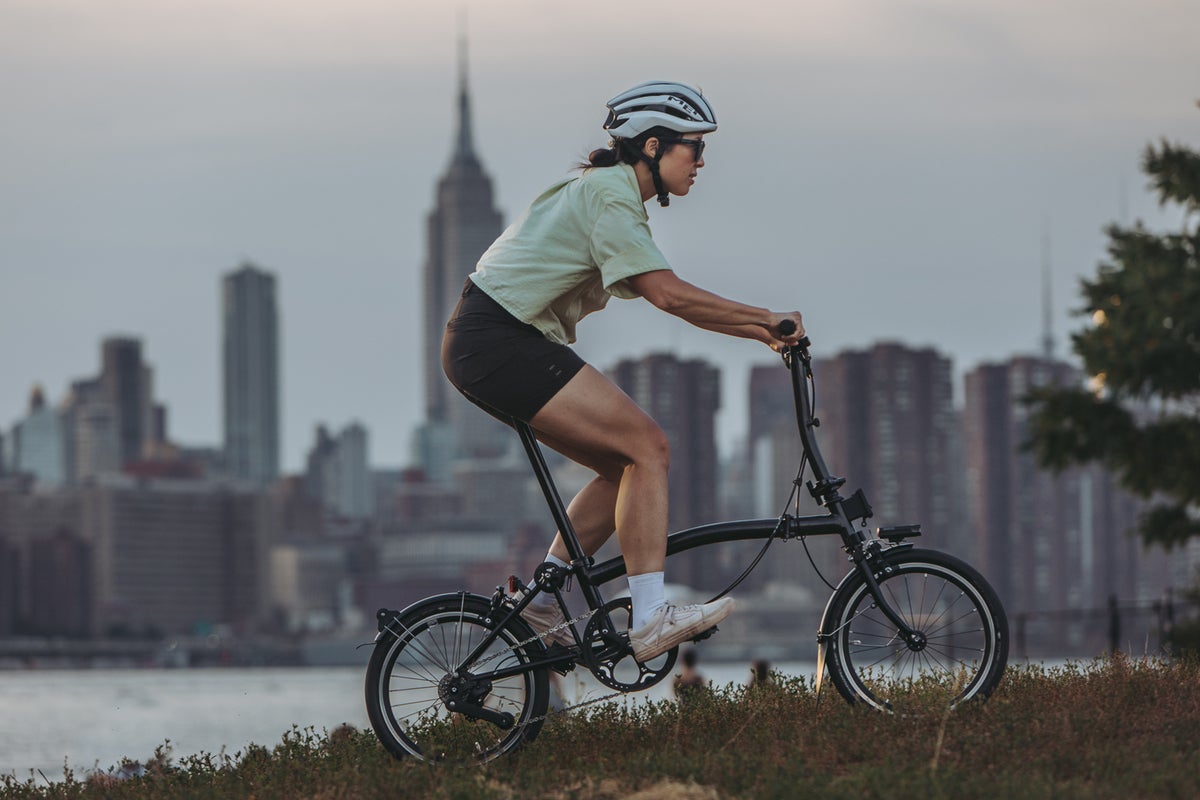 A woman riding a lightweight Brompton P Line folding bike through a park in NYC