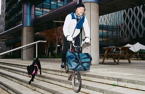 Hombre en una bicicleta Brompton con una perra negra