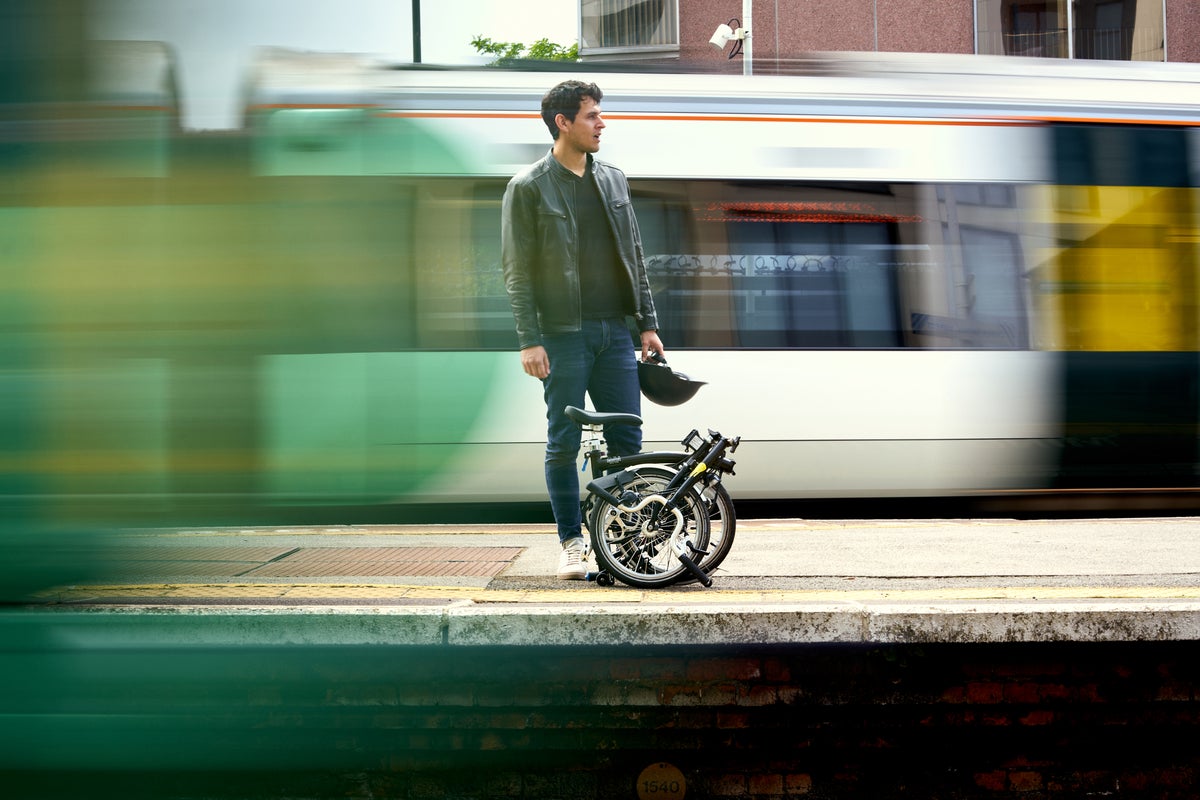 man stood on train platform with folded brompton bike