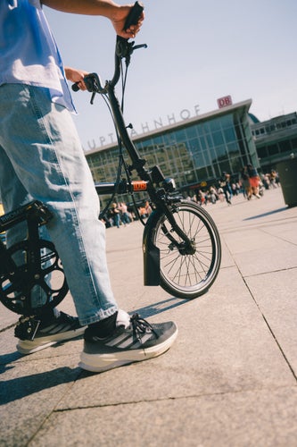 model stood with a brompton bike in front of station in germany