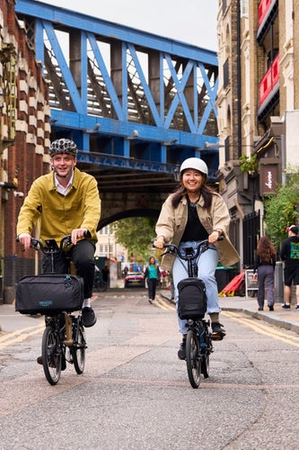 Zwei glückliche Menschen fahren mit Brompton Electrics durch London