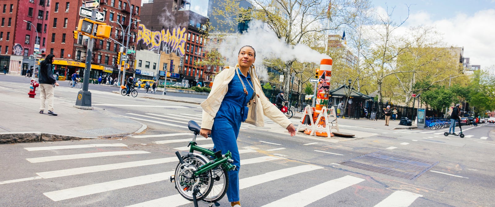 A woman carrying a folded Forest Green Brompton across the street of NYC