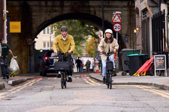 two people riding brompton bikes near a railway arch