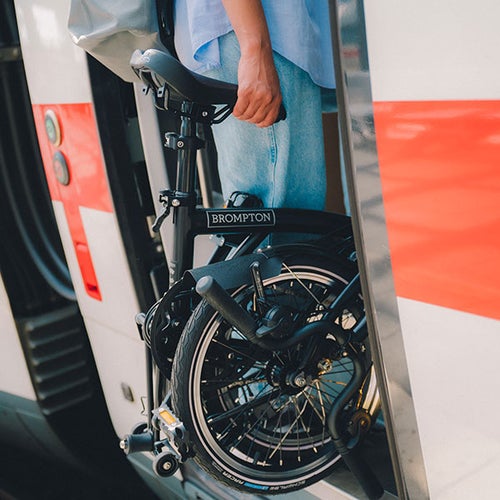 Person carrying folded Brompton bike onto a train