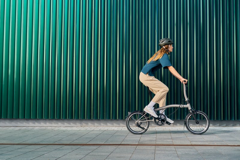 person riding a brompton t line bike in front of a green wall