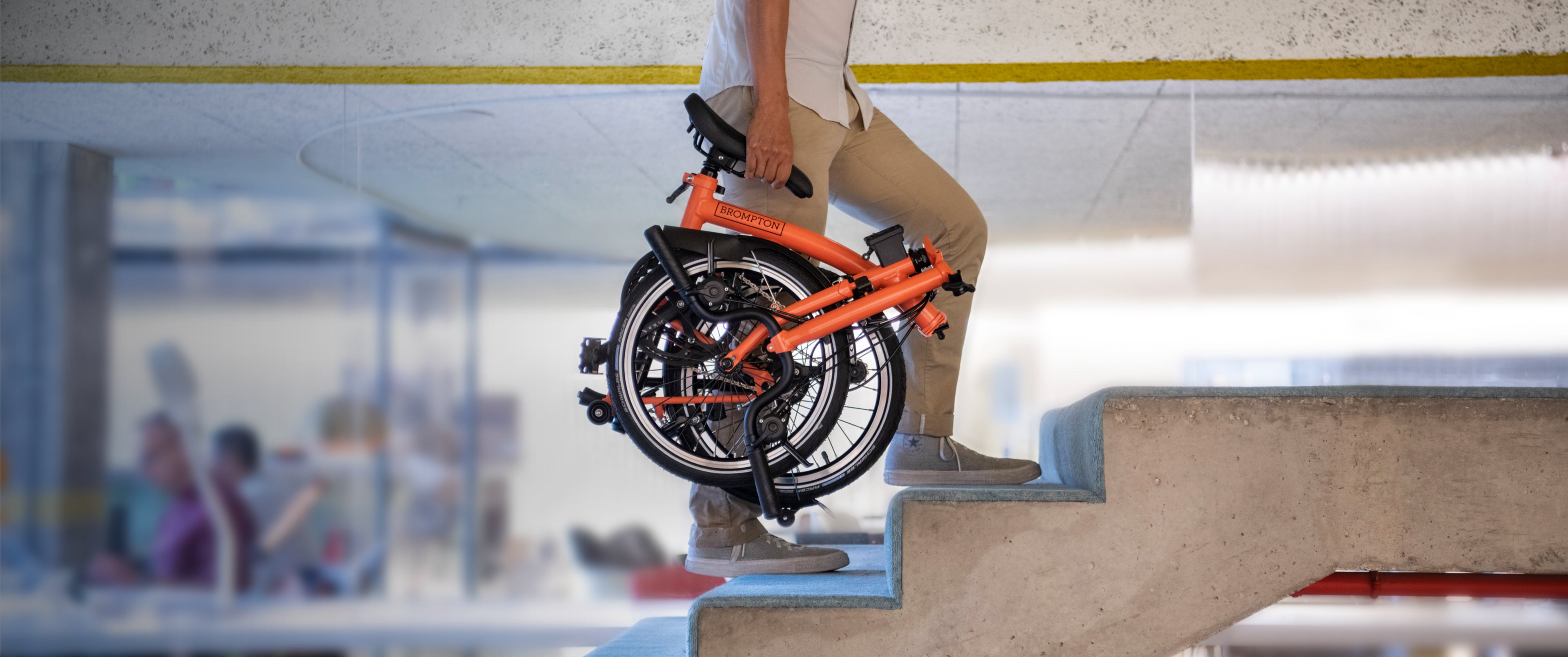 A person carrying a folded Brompton C Line up a flight of stairs