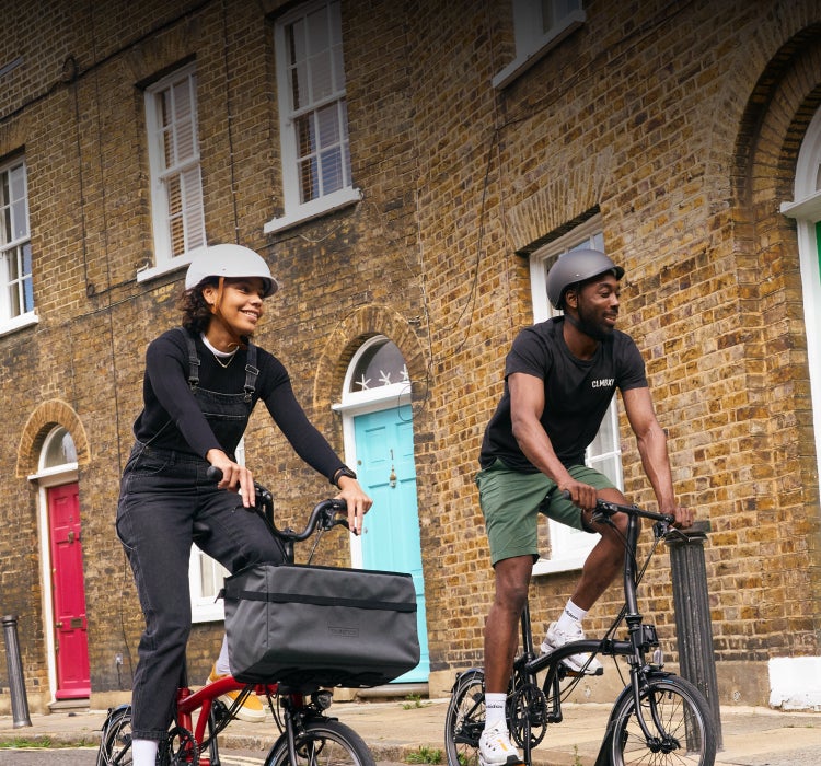 Two happy people riding Brompton folding bikes through a beautiful street