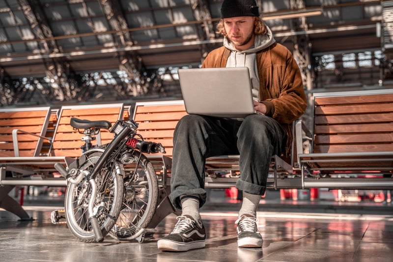 person on laptop with folded brompton bike next to them