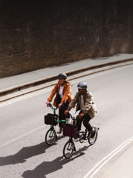Zwei Leute, die mit Brompton-Fahrrädern auf der Straße unterwegs sind