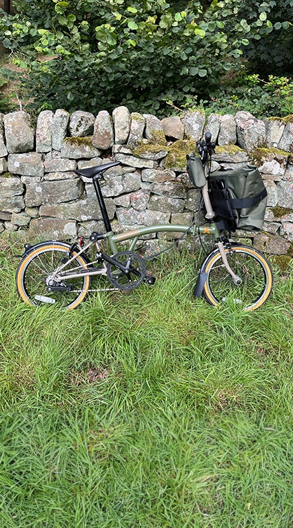 A Brompton x Bear Grylls bike leaning against a stone wall