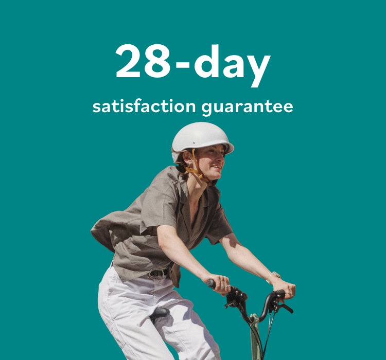 A happy woman riding a Brompton Matcha Green folding bike against a graphic green background with white graphic text "28-day satisfaction guarantee"