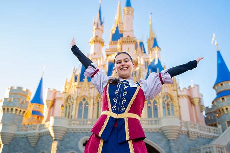 Female Disney International Programs participant in costume smiling with her arms up in the air in front of Cinderella's Castle at Walt Disney World Resort's Magic Kingdom