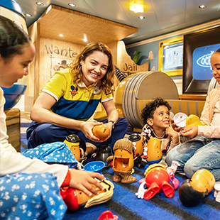 female nursery counselor in uniform, smiling and helping a small group of children play with Mr. Potato Head toys