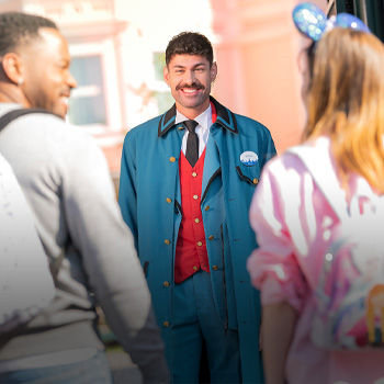 A Disney cast member with a mustache greets park guests