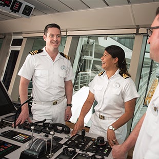 small group of smiling deck officers in white uniforms, inside a ship's control room