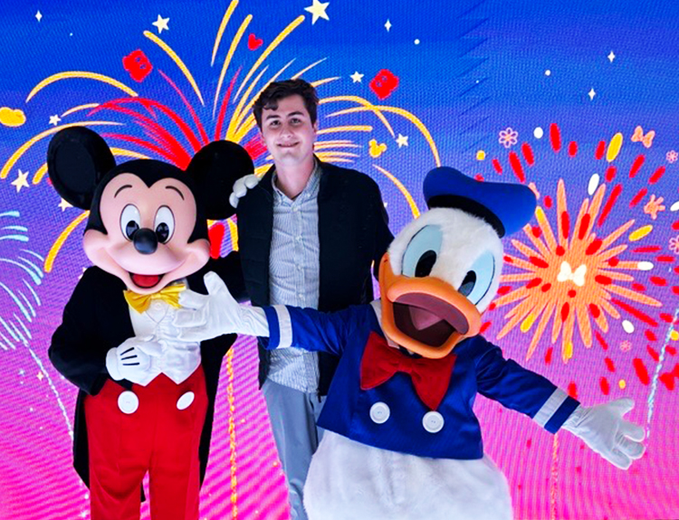 Mexico intern Guillermo wearing a collared shirt, blazer and jeans, smiling with Mickey Mouse and Donald Duck