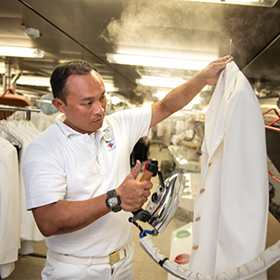 male dry cleaning specialist in uniform, ironing a white chef coat