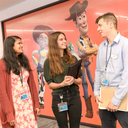 Three colleagues converse against a vibrant Toy Story backdrop