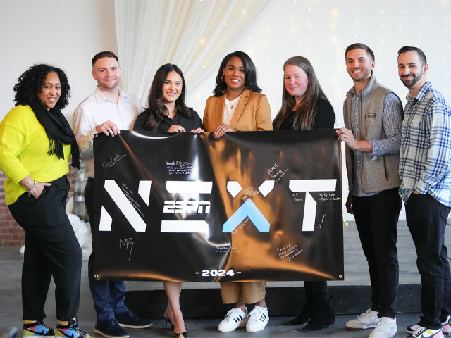 A group of seven ESPN NEXT participants holding a black banner that reads "NEXT 2024"