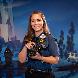 female photographer smiling and holding a camera in front of a Disney castle backdrop