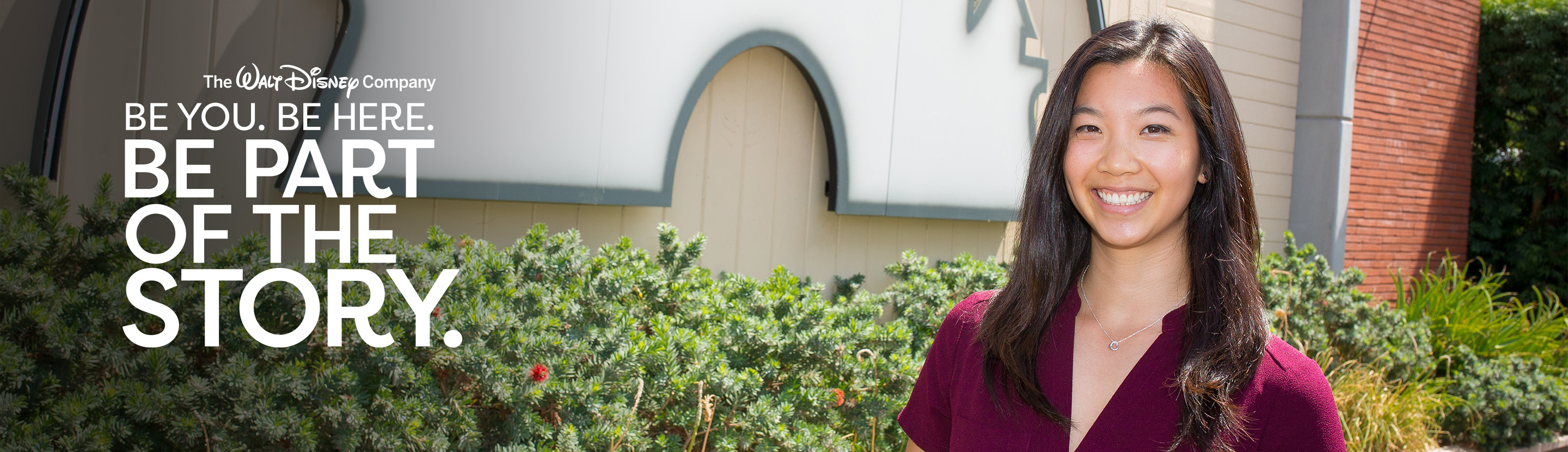 A smiling young woman with long dark hair stands outdoors