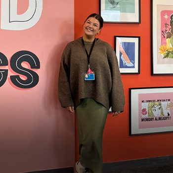 A smiling woman in a casual outfit stands against a vibrant, art-decorated wall