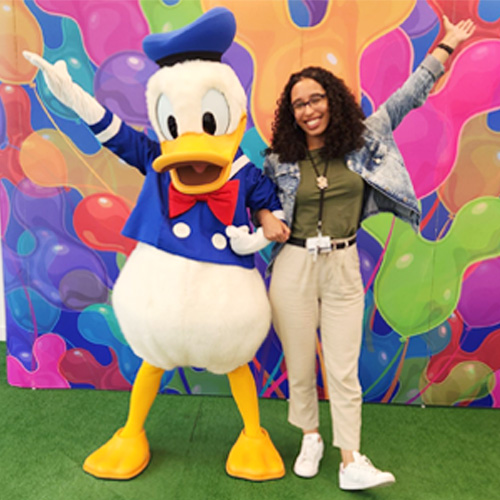 Person standing beside Donald Duck against a colorful mural backdrop at a theme park