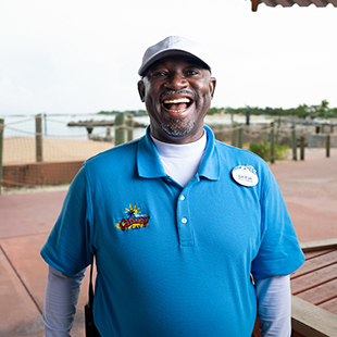 black male security guard, standing in front of a beach and smiling