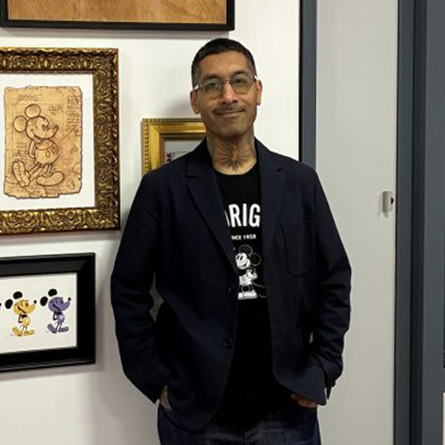 Employee posing next to a wall displaying framed Disney artwork and sketches