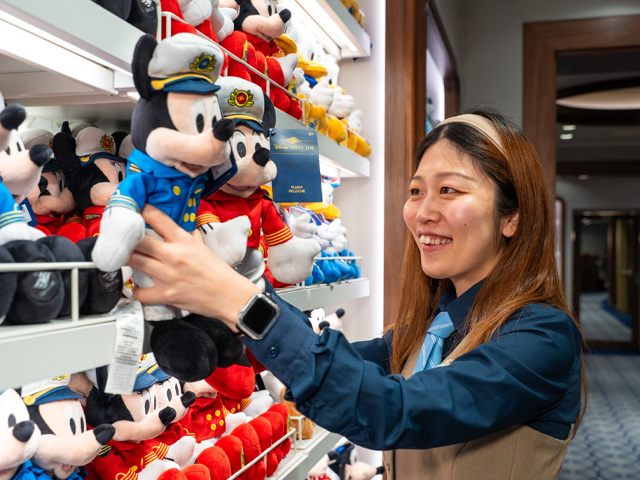 Smiling employee placing a plush Mickey and Minnie Mouse on a shelf
