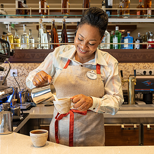 female bartender in uniform, preparing a cup of coffee behind a bar