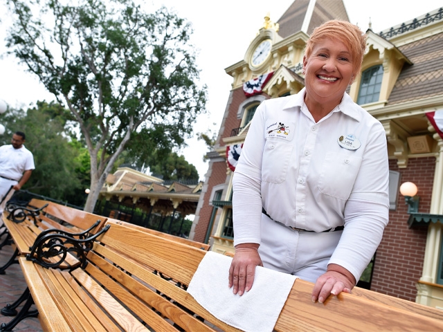 A smiling Disney cast member in a white uniform cleaning a bench