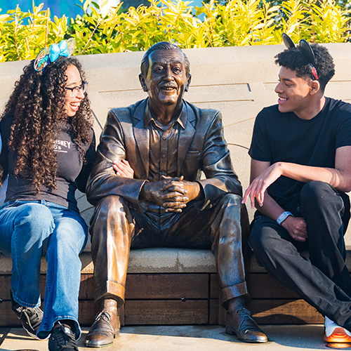 2 young people sitting next to a statue of Walt Disney