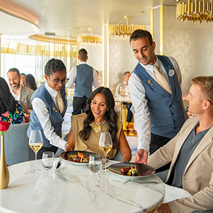 a male and a female server serving dishes to a couple seated at a dining table