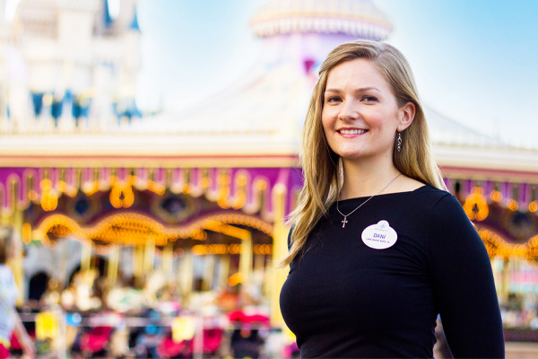 Cast member posing near Prince Charming Regal Carrousel with Fantasyland attractions in the background