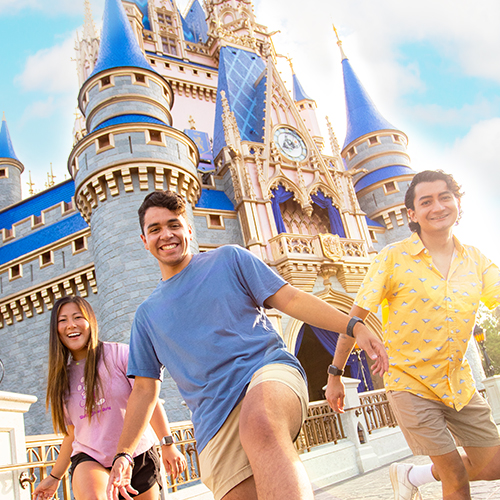 3 young people smiling and linking arms in front of a Disney castle