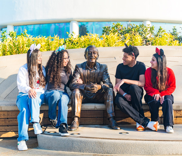 Young people in Mickey Mouse ears pose with a Walt Disney statue