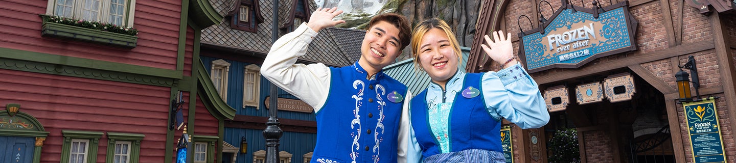 pair of colleagues in costumes waving in front of the Frozen Ever After ride at Hong Kong Disneyland Resort