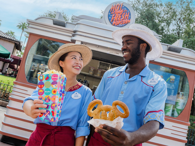 Description Smiling cast members serving up popcorn and a Mickey pretzel at a Disney park