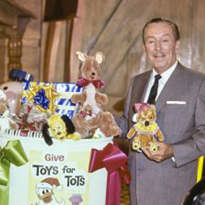 Walt Disney standing beside a Toys for Tots donation display featuring stuffed animals and donated toys