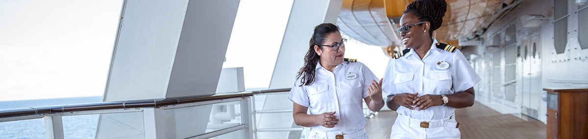 hispanic female and black female crew member walking along a ship deck and conversing