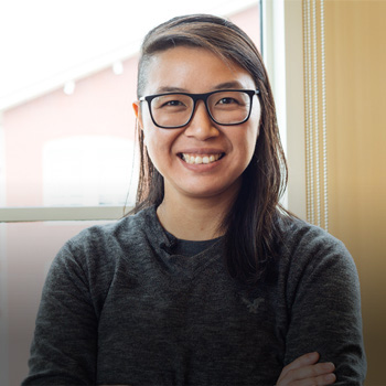 A smiling person wearing glasses with a partially shaved haircut