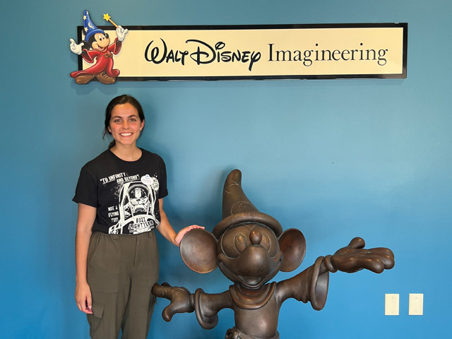 A woman smiles next to a Sorcerer Mickey statue at Walt Disney Imagineering
